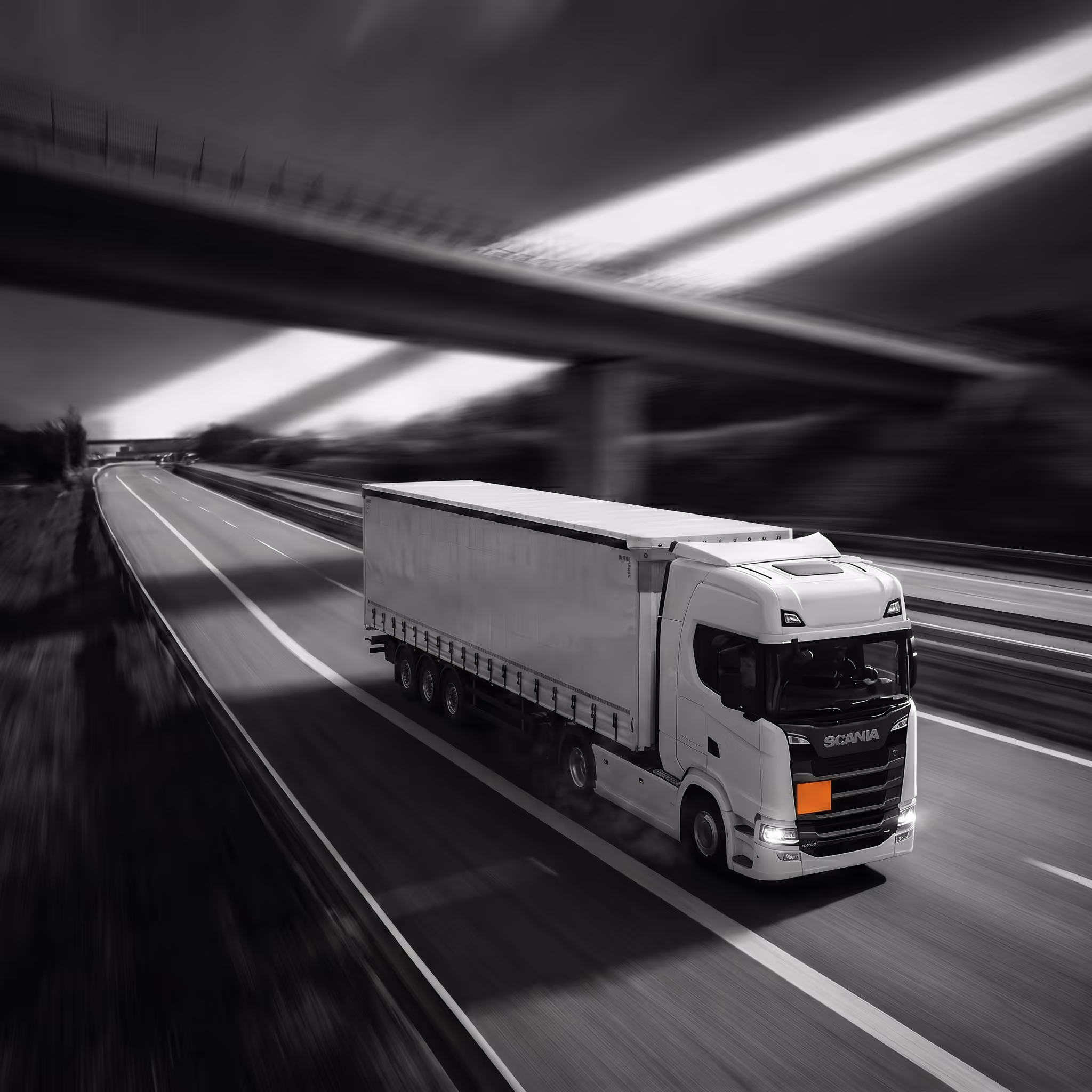 White Scania semi-truck on it driving fast on empty highway under an overpass in black and white with ADR palting on it.